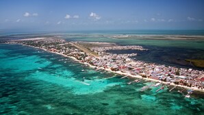 An aerial view of a coastal town with clear turquoise waters, a marina with boats, and a densely built urban area with buildings and roads. - Casual & Comfortable Belize Beach House: Private Pool, Dock, & Secluded Privacy
 (San Pedro)