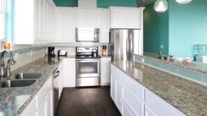 Una cocina moderna con armarios blancos, electrodomésticos de acero inoxidable y paredes color turquesa.