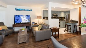 Ein modernes Wohnzimmer mit Flachbildfernseher, Ledersofas, einem Couchtisch und einer Küchenzeile mit Barhocker.