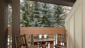 Ein Balkon mit einem Holztisch und zwei Stühlen mit Blick auf einen verschneiten Wald.