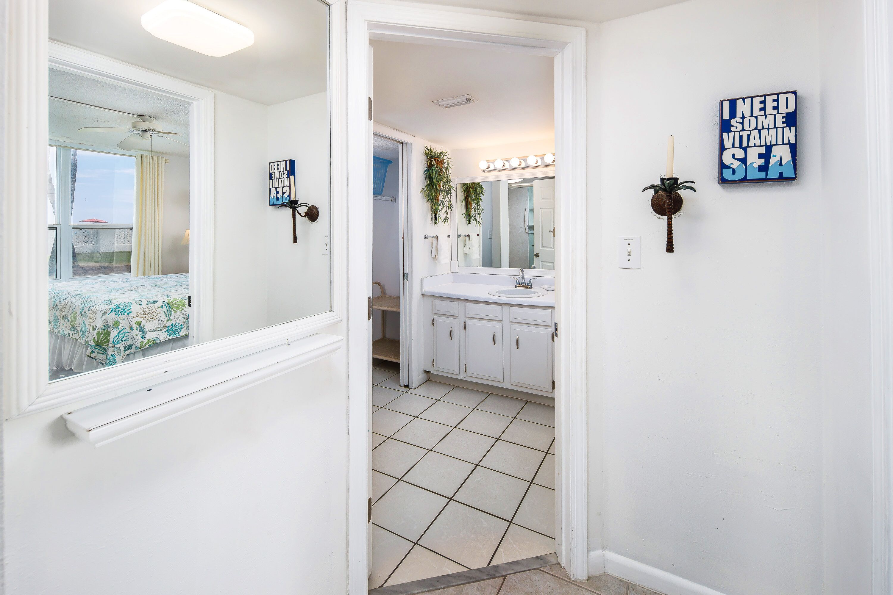 Un couloir d’hôtel avec une salle de bain équipée d’un grand miroir, d’un lavabo et de placards.