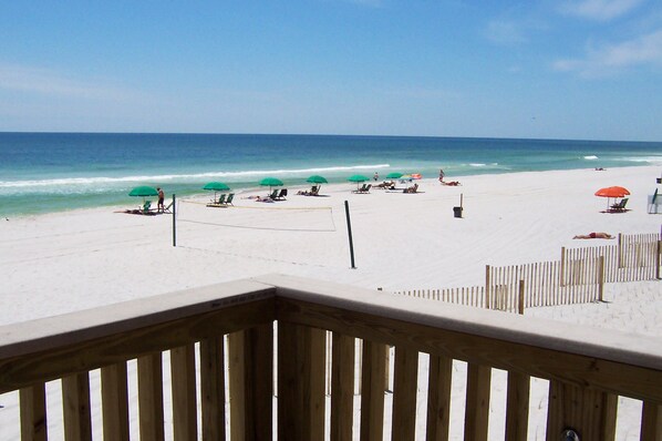 A beach with multiple umbrellas and lounge chairs, a wooden fence, and a clear view of the ocean.