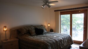 Un dormitorio con una cama, dos lámparas de noche, un ventilador de techo y un ventanal corredero al exterior.