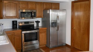Una cocina con armarios de madera, un refrigerador de acero inoxidable, un microondas, un horno y una cafetera.