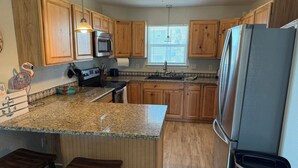 A kitchen with wooden cabinets, granite countertops, a stainless steel refrigerator, and a built-in oven. - The Beach and Surf is Just Steps Away! (Surfside Beach)