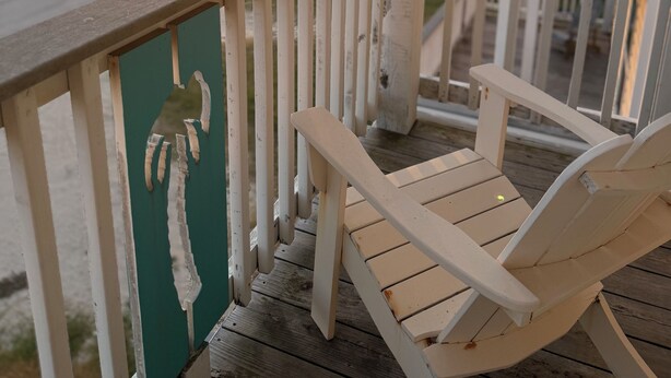 A wooden deck with a white railing, a green wall with a palm print, and a white chair. - The Beach and Surf is Just Steps Away! (Surfside Beach)