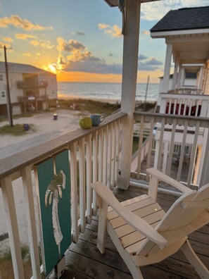 A wooden deck with a white railing, a green wall with a palm print, and a white chair. - The Beach and Surf is Just Steps Away! (Surfside Beach)