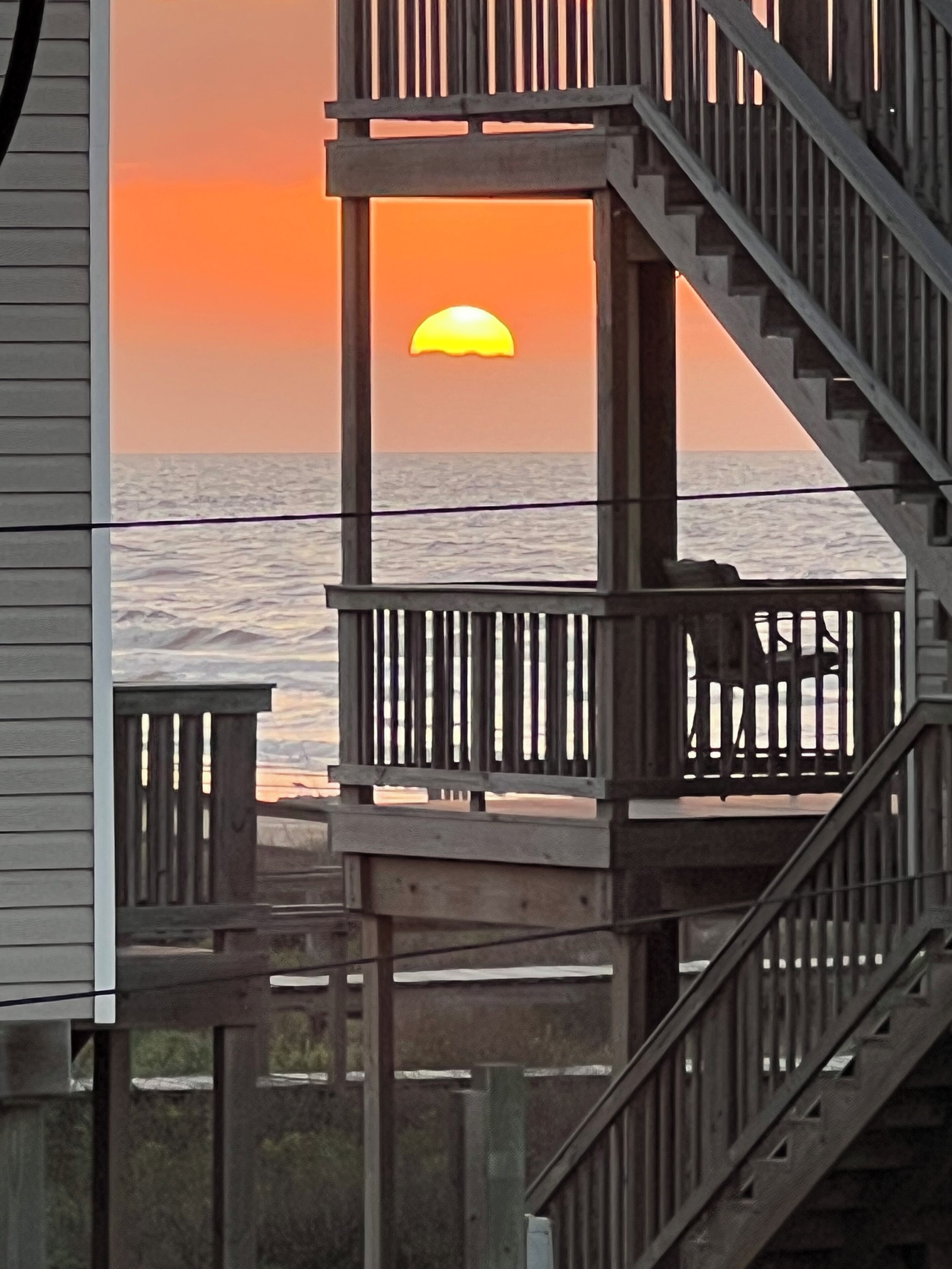 Eine Holzterrasse mit Geländer, die auf den Sonnenuntergang über dem Meer hinausblickt.