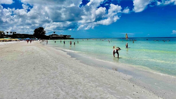 A beach with clear turquoise water, people swimming and walking along the shore, and a sailboat in the distance. - VILLA 4, Siesta Key, Walk to Beach. Pool. Daily Rentals (Sarasota)