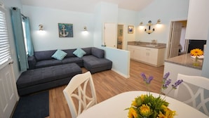 A modern living room with a grey sectional sofa, a dining table with a vase of flowers, and a kitchen area with white cabinets and a granite countertop. - VILLA 4, Siesta Key, Walk to Beach. Pool. Daily Rentals (Sarasota)