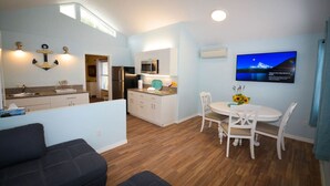A modern kitchen with white cabinets, a stainless steel refrigerator, and a microwave. There is a dining area with a white table and chairs, and a TV mounted on the wall displaying a scenic view. - VILLA 4, Siesta Key, Walk to Beach. Pool. Daily Rentals (Sarasota)