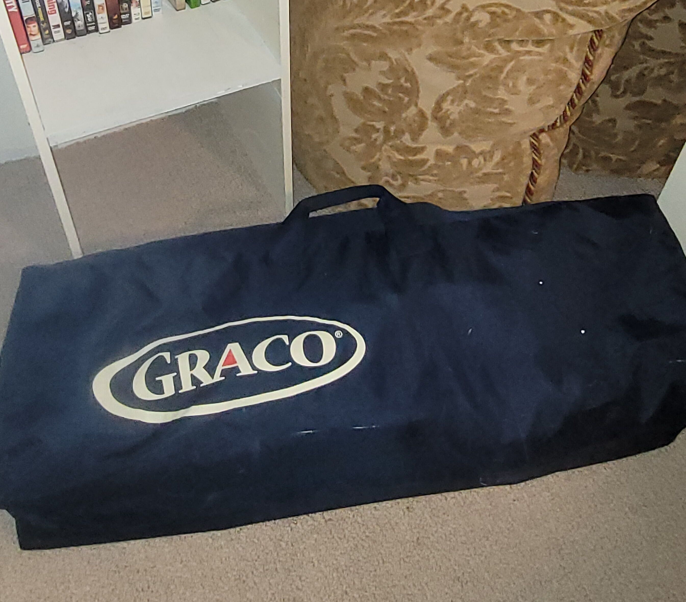 Una bolsa GRACO azul oscuro con un logotipo sobre un piso alfombrado.