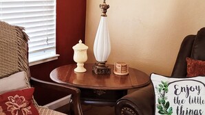 Uma sala de estar acolhedora com um sofá de couro marrom, uma poltrona estampada e uma pequena mesa redonda com uma luminária e objetos decorativos.