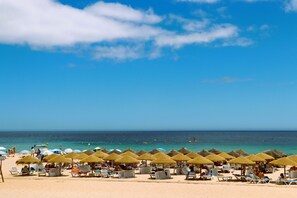 Een strand met rijen ligbedden en rieten parasols.