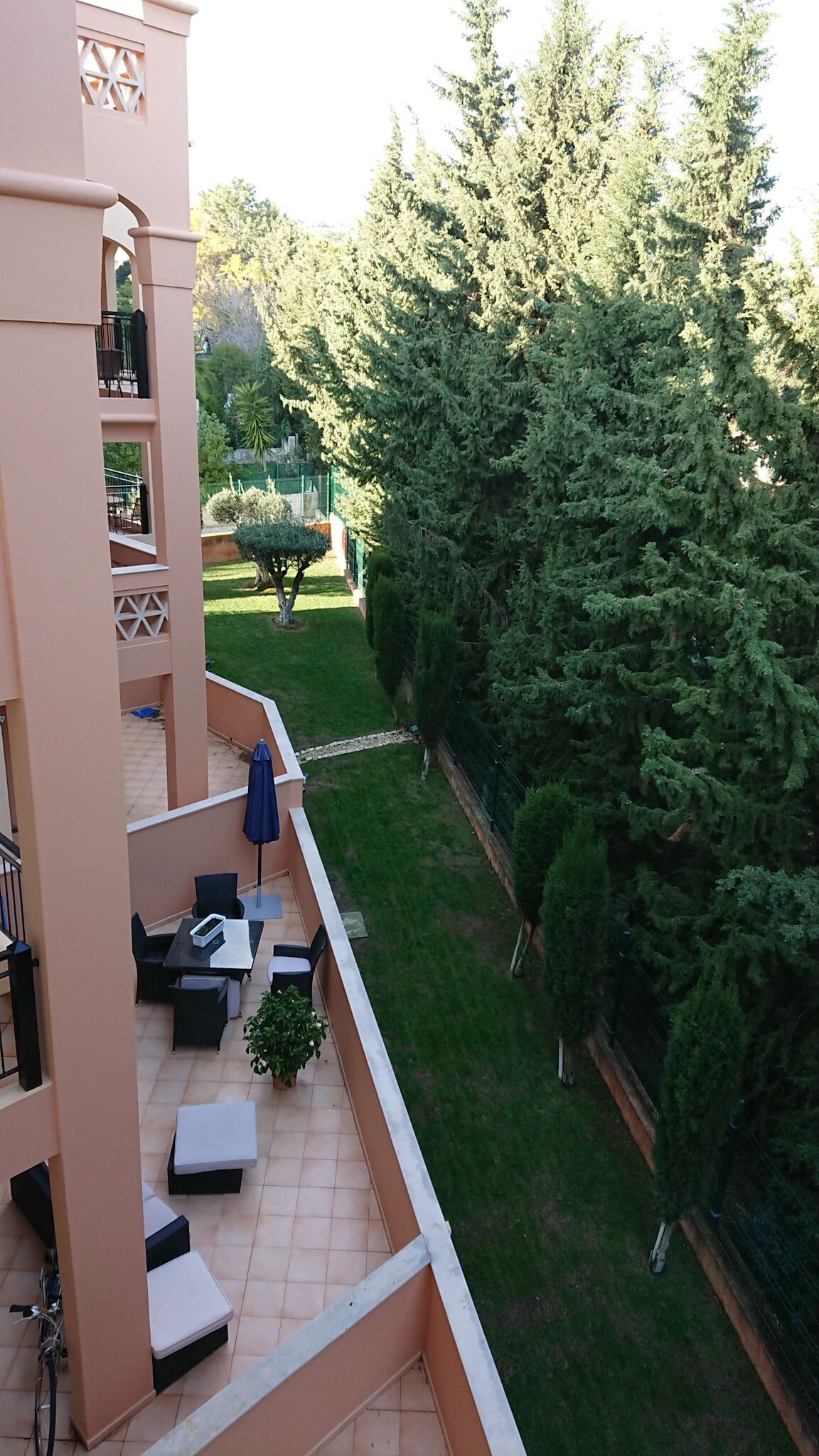 A balcony with outdoor seating and a view of a well-maintained garden and trees.