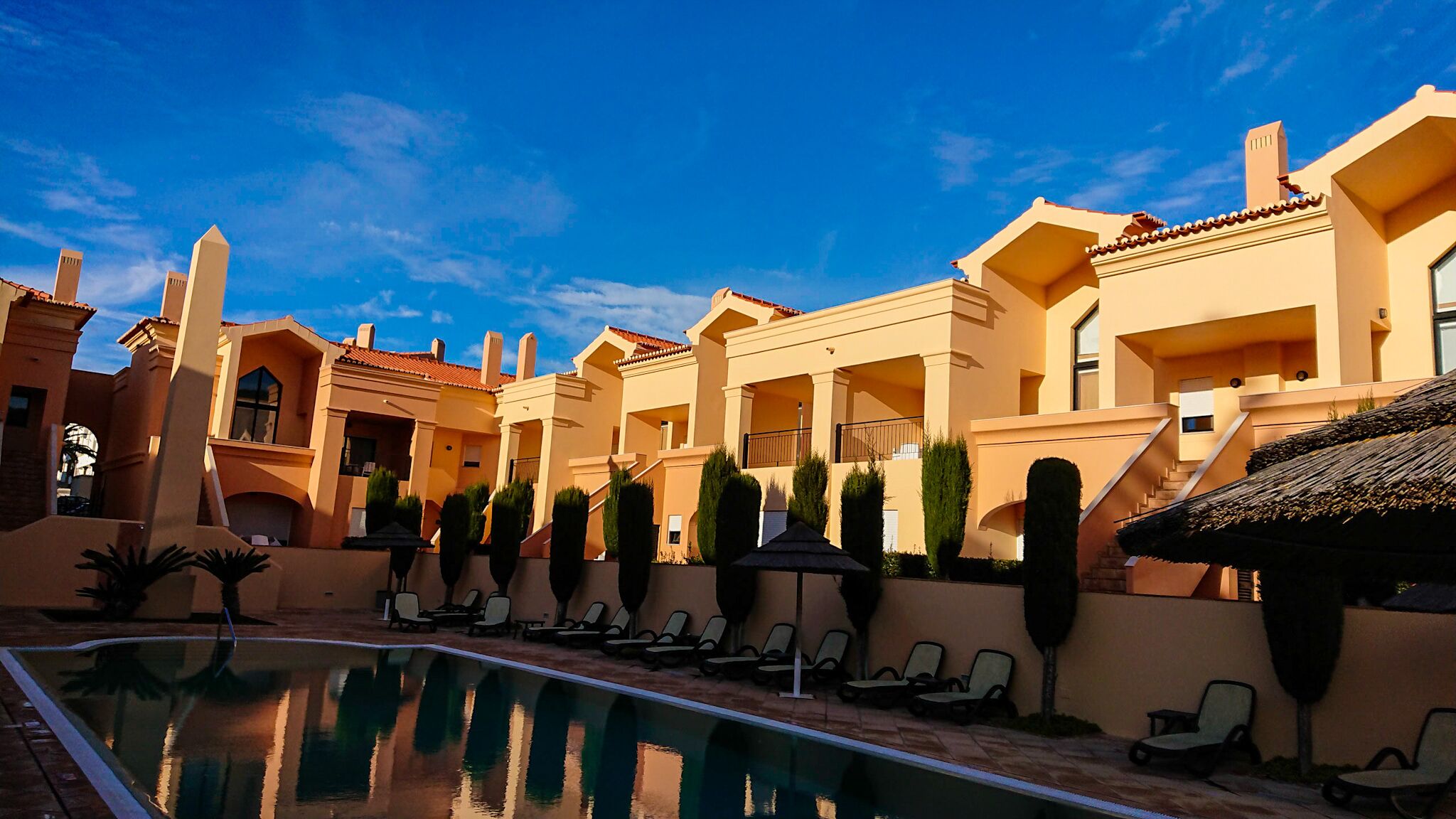 Un resort con piscina, sillas de descanso y un cielo azul despejado.