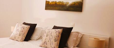 A bedroom with a bed, pillows, a bedside lamp, and a painting on the wall.