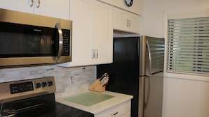 Cozinha com armários brancos, geladeira preta, micro-ondas de aço inoxidável e fogão.