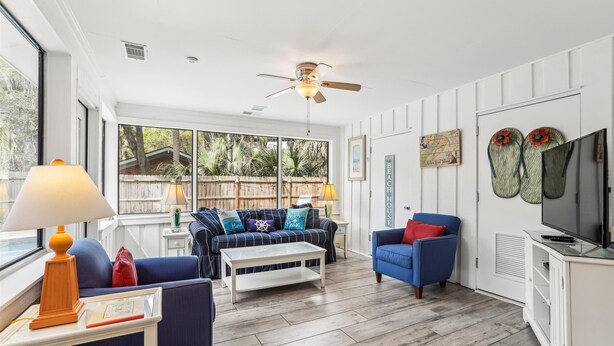 A spacious living area with a ceiling fan, a large window offering a view of the outdoors, and a television on a cabinet. - Pup Friendly Home w/ Fully Fenced Yard! (Hilton Head Island)