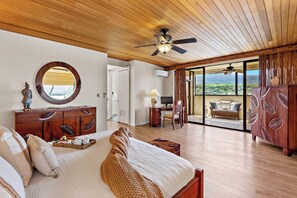 A bedroom with a bed, wooden ceiling, a round mirror, a dresser, a desk with a chair, and a balcony with a view.