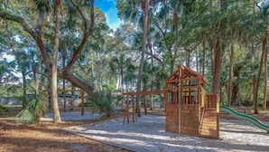 A playground with climbing structures and a slide, surrounded by trees. - Pet Friendly 3BR w/ Screened Porch & Amenities (Hilton Head Island)