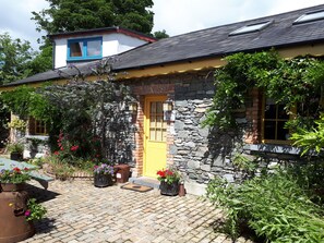 A stone house with a yellow door, surrounded by potted plants and a cobblestone patio.