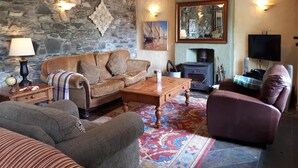Un salon chaleureux avec un mur en pierre, une cheminée, un téléviseur et des fauteuils confortables.