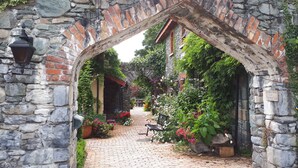Un arc en pierre mène à un sentier pavé de pierres, bordé de plantes et de fleurs en pot.