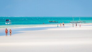 Ein Strand mit Menschen, einem Boot und ruhigem türkisblauem Wasser.
