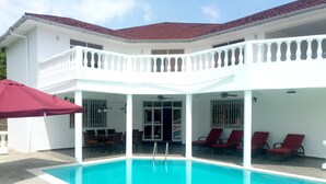 Ein Poolbereich mit einem weißen Gebäude, einem roten Sonnenschirm und roten Liegestühlen.