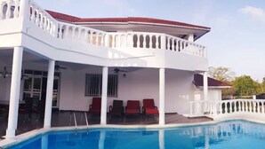 Ein zweigeschossiges Gebäude mit Schwimmbad, roten Liegestühlen und einer überdachten Terrasse.