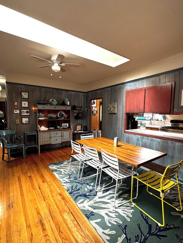 A dining area with a wooden table and chairs, a ceiling fan, and a kitchen area with cabinets and appliances.