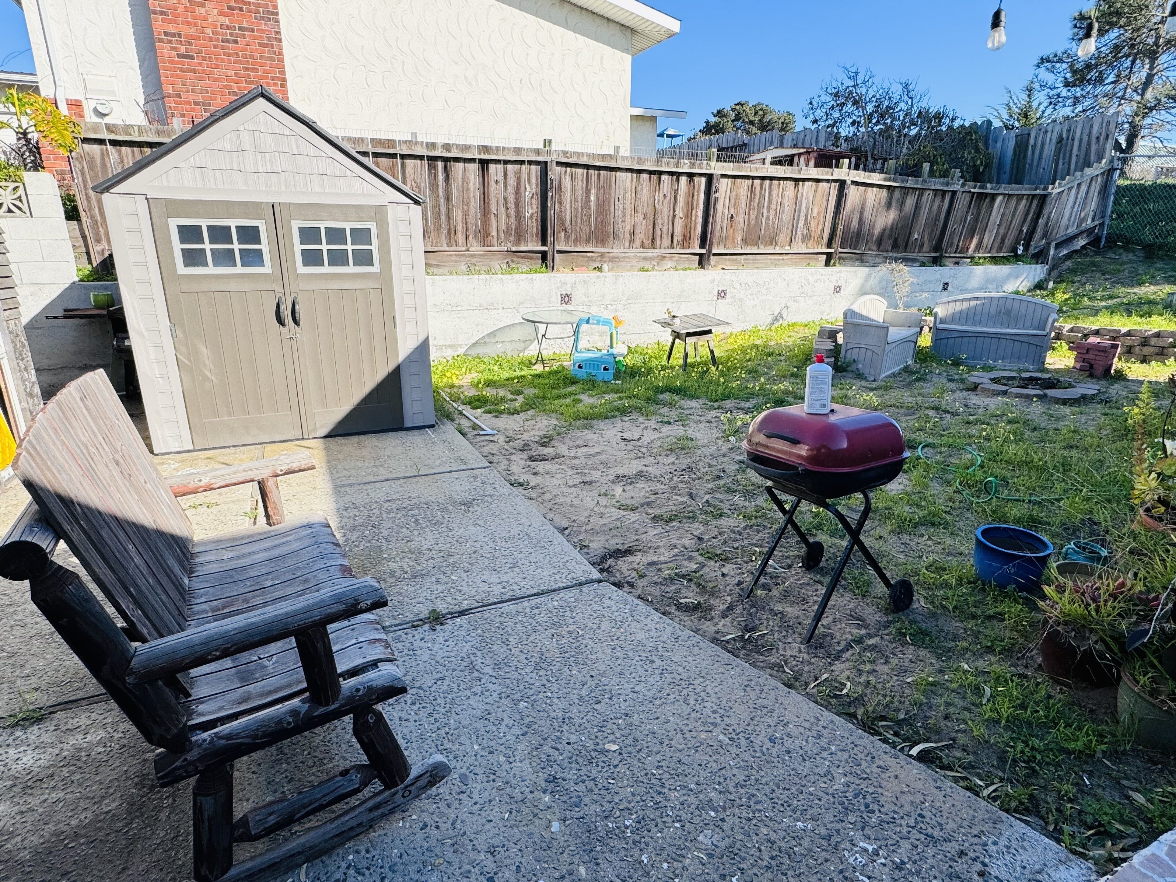 Un patio trasero con un banco de madera, una parrilla, un cobertizo y un área cercada.