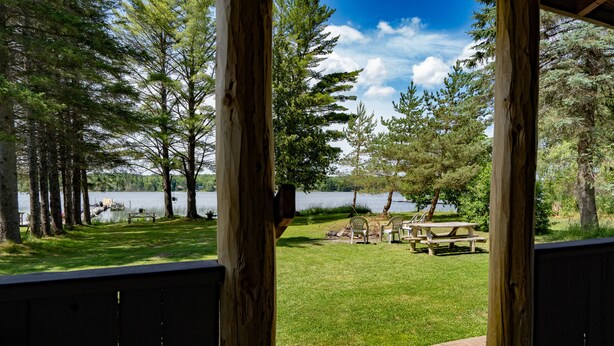 Terraza de madera con vista a un espacio cubierto de césped, mesas de picnic y un lago.