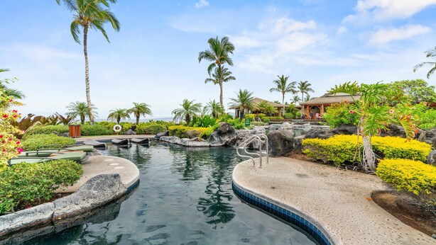 A pool area with a water feature, palm trees, and a covered seating area.