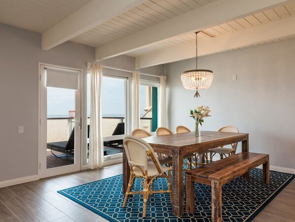 Un coin repas avec une table en bois, des chaises et un banc. Un lustre est suspendu au-dessus de la table.