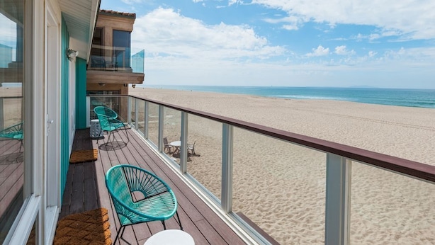 Ein Balkon mit Blick auf den Strand, eine Holzterrasse und zwei grüne Stühle.