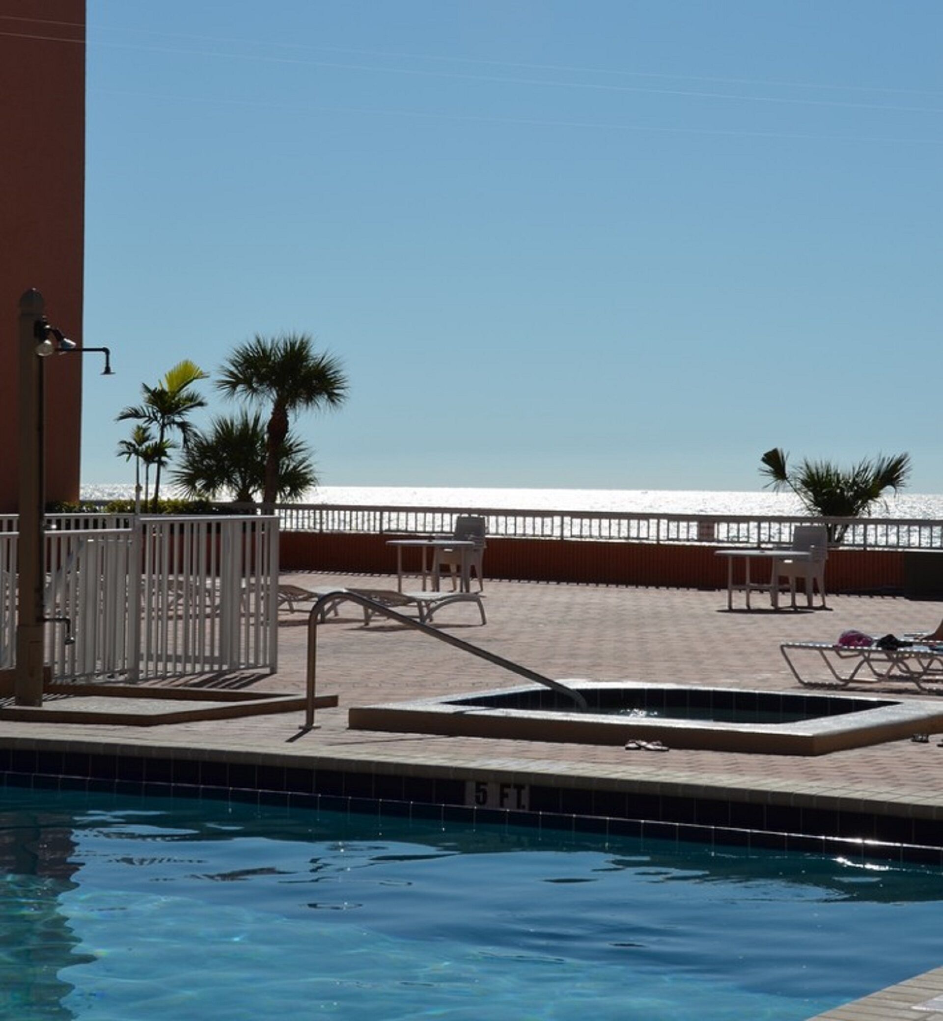 A pool area with lounge chairs, a small pool, and a view of the beach.