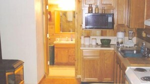 A compact kitchen with wooden cabinets, a microwave, a stove, and a coffee maker. - West Yellowstone Cabin (West Yellowstone)
