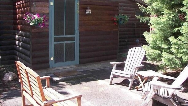 A log cabin with a wooden door, two Adirondack chairs, and a small porch area. - West Yellowstone Cabin (West Yellowstone)