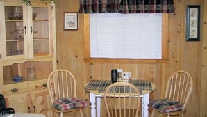A wooden interior with a dining table and chairs, a clock, a window with blinds, and a cabinet with glass doors. - West Yellowstone Cabin (West Yellowstone)
