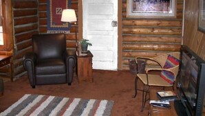 A log cabin interior with a leather chair, a small table with a lamp, a television, and a framed picture on the wall. - West Yellowstone Cabin (West Yellowstone)
