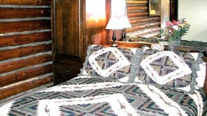 A log cabin room with a bed, a nightstand, a lamp, and a mirror. - West Yellowstone Cabin (West Yellowstone)