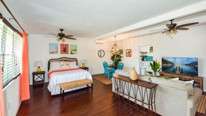 A well-lit room with a bed, a desk, a TV, and ceiling fans. - Comfy Beach Studio for 2 - Only a short walk to the beach. (Cape Canaveral)