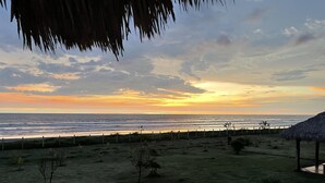A beach view with a fence, a thatched structure, and sparse vegetation.