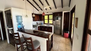 A kitchen with a central island, wooden chairs, a water dispenser, a stove, and a refrigerator.