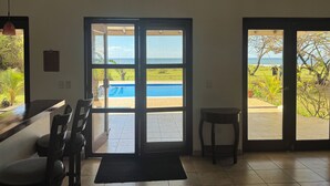A room with a view of a pool and ocean, featuring a door leading outside, a chair, and a small table.