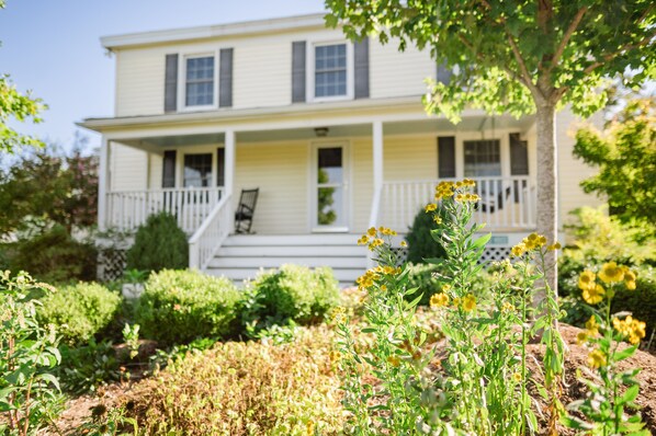 A two-story house with a porch, steps leading to the front door, and a garden with yellow flowers. - South River Guest House (Stanardsville)
