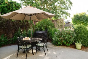 An outdoor patio with a round table, four chairs, a large umbrella, and a grill. - South River Guest House (Stanardsville)