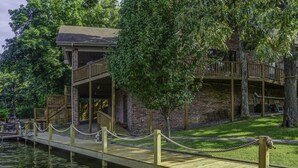 A wooden dock leading to a brick building with a balcony, surrounded by trees. - Centrally Located Lake House with a Secluded Feel Boat Slip Included (HOT SPRINGS NATIONAL PARK)
